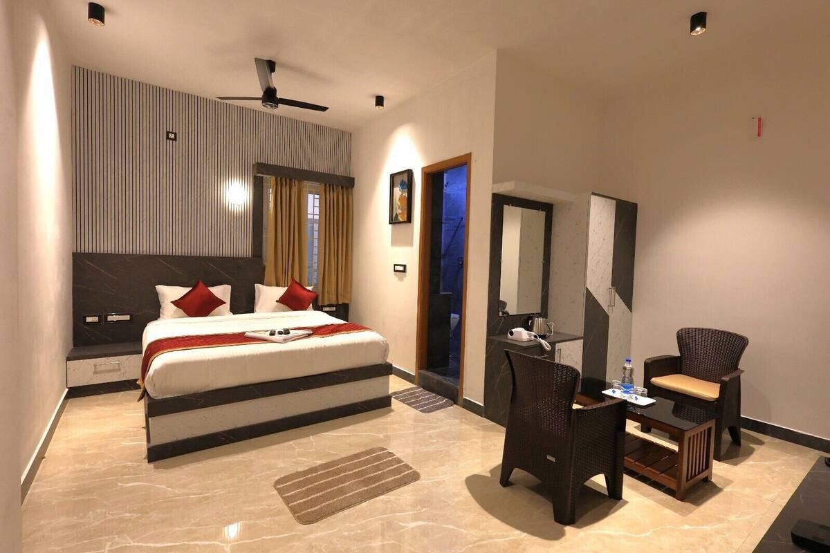 A modern hotel room with a large bed, a desk with a chair, a mirror, and a ceiling fan.
