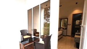 A room with a glass partition, wicker furniture, a bed, and a bathroom visible through the partition. - Ozone Hill Resorts (Yercaud)