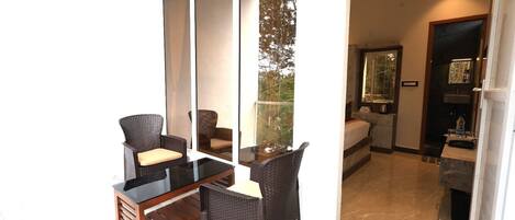 A room with a glass partition, wicker furniture, a bed, and a bathroom visible through the partition.