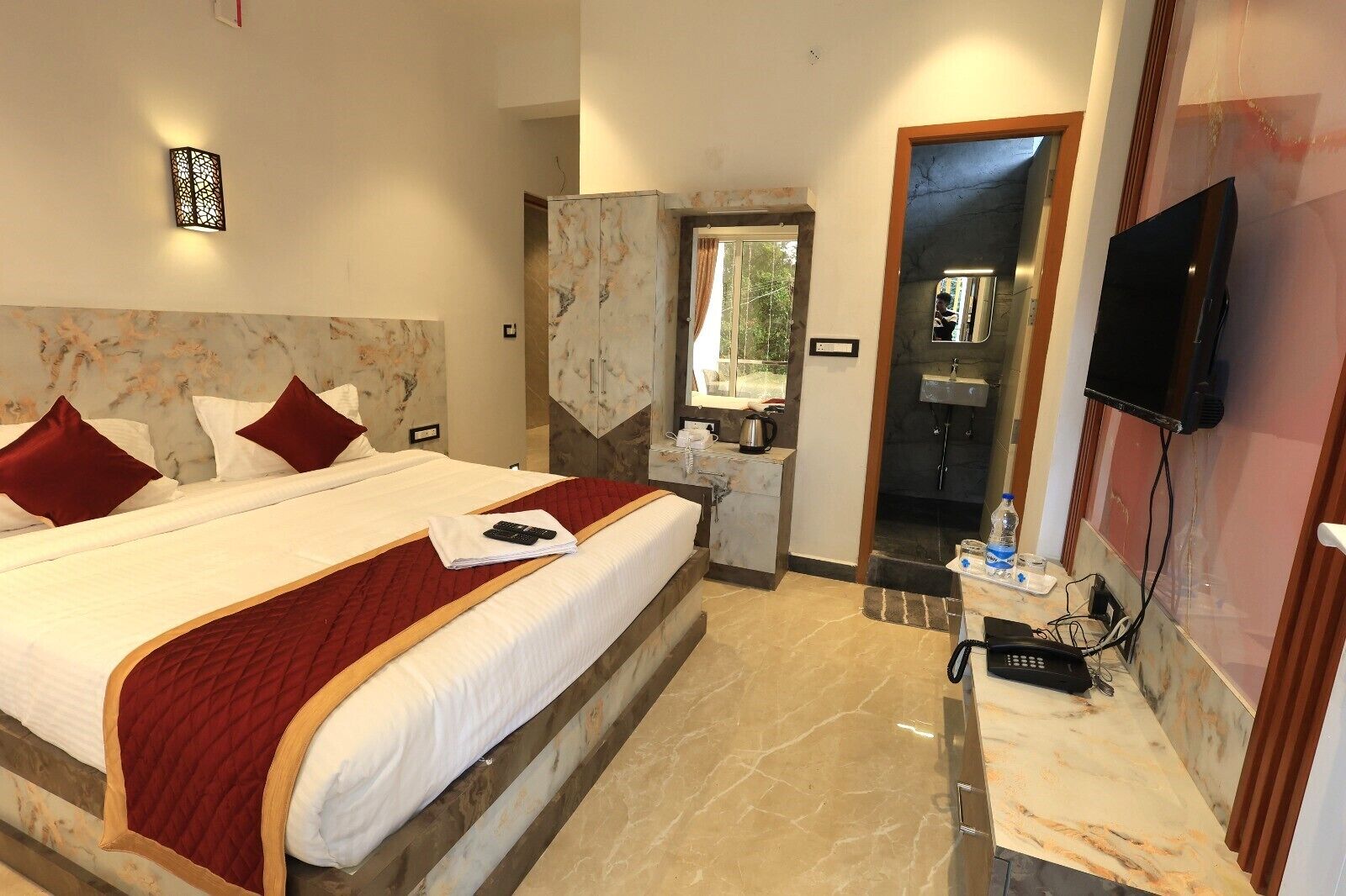 Een hotelkamer met een groot bed, een televisie, een badkamer met een wastafel en een spiegel.