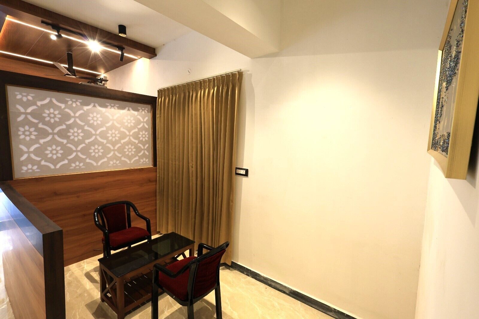 A small, modern room with a wooden table and two chairs, a large window with curtains, and a decorative wall panel.
