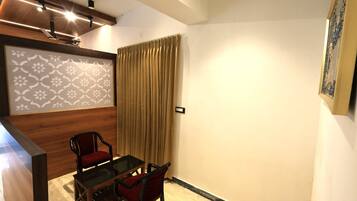 A small, modern room with a wooden table and two chairs, a large window with curtains, and a decorative wall panel.
