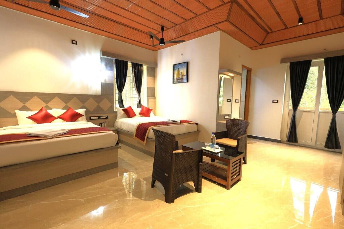 A hotel room with two beds, a sitting area with a table and chairs, and large windows with curtains.