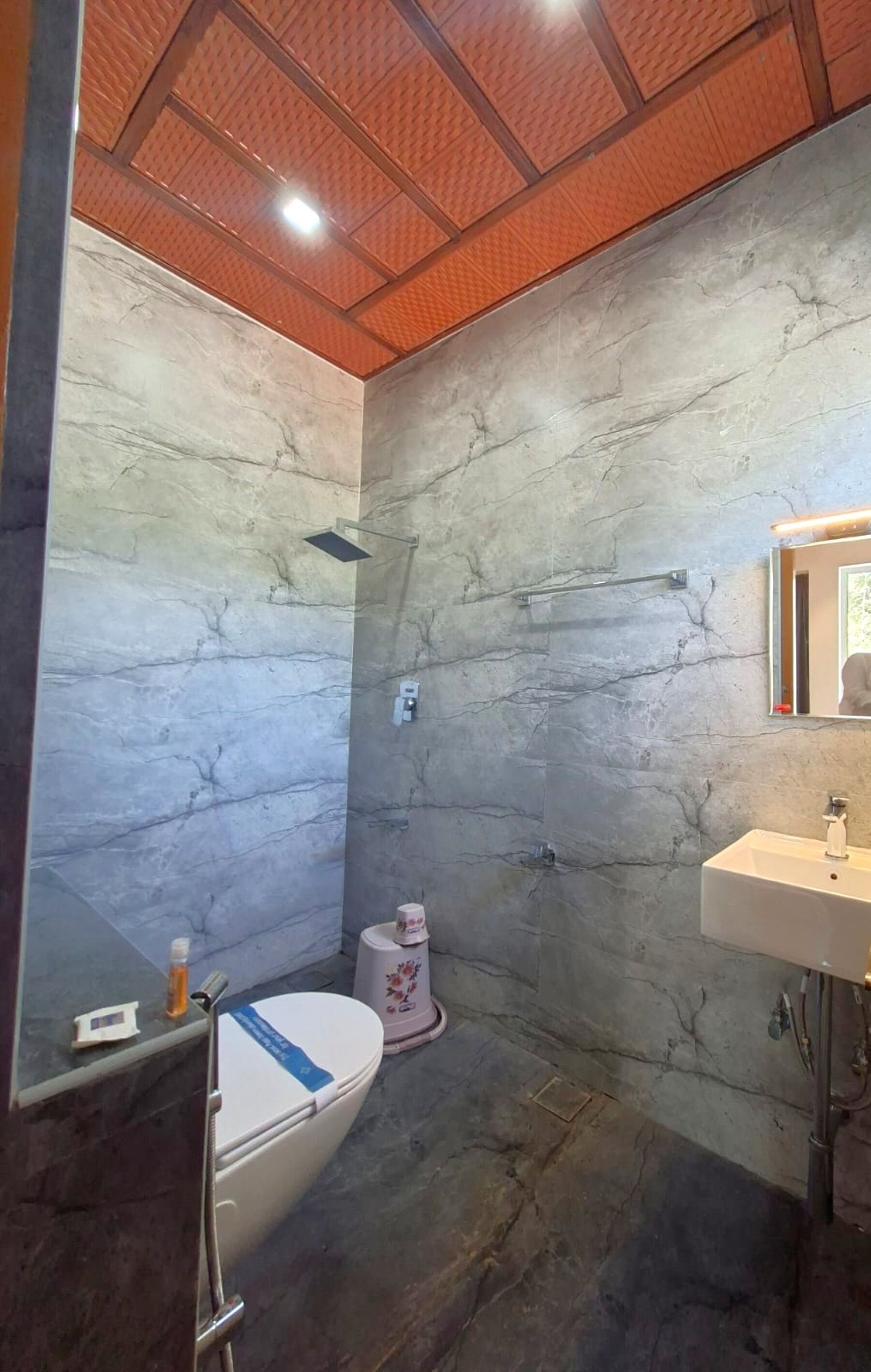 A bathroom with a marble wall, a toilet, a sink, and a shower.