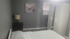 Een slaapkamer met een bed, een nachtkastje met een lamp, een kledingkast en een raam met jaloezieën.