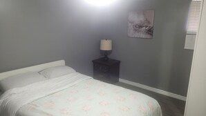 Een slaapkamer met een bed, een nachtkastje met lamp en een aan de muur hangend schilderij.