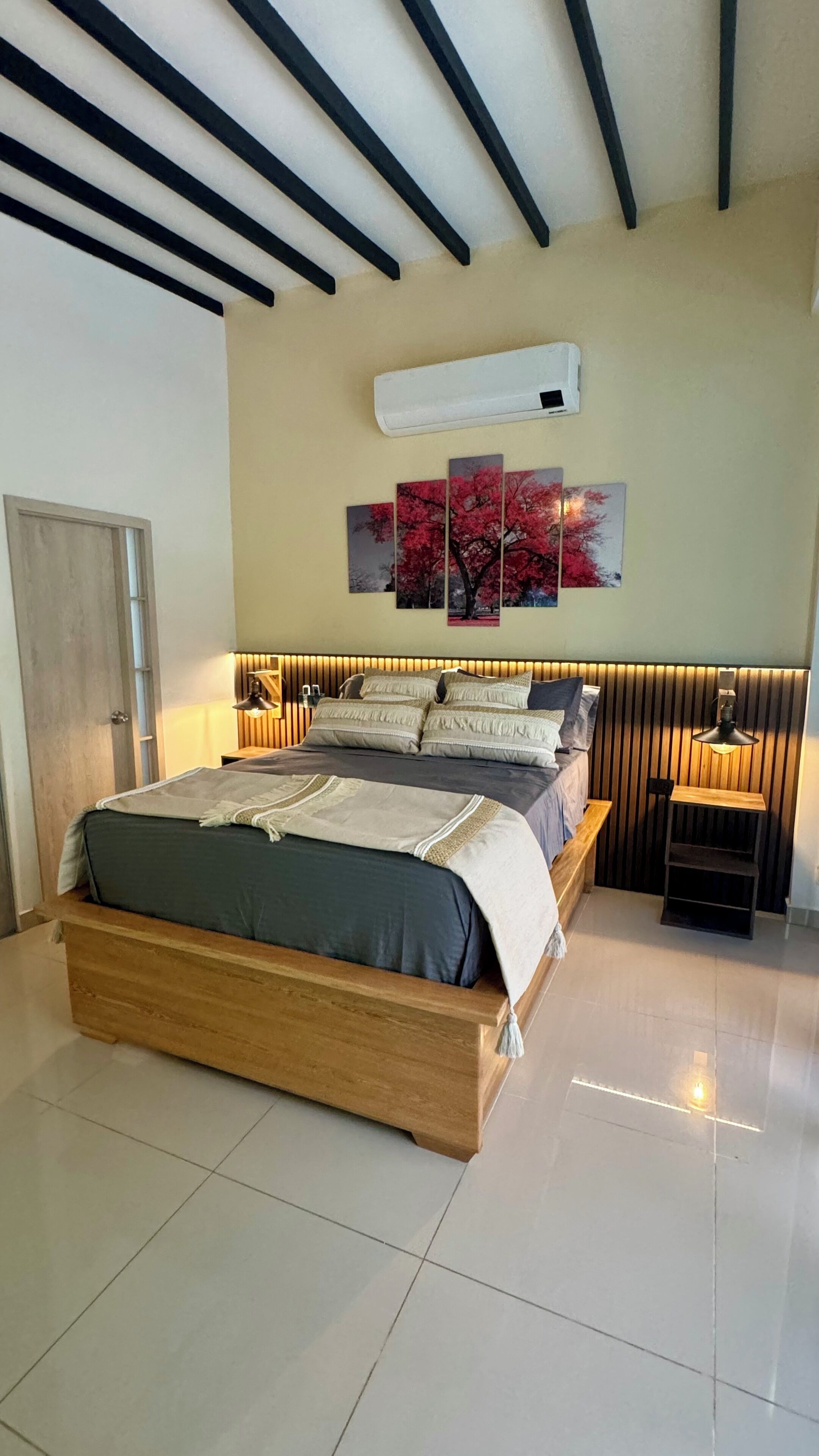 Una camera da letto moderna con un letto grande, un comodino, un condizionatore d'aria a parete e un elemento decorativo al muro.