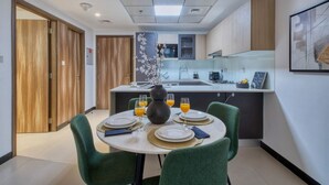 A modern kitchen with a central island, wooden cabinets, and a dining area with green chairs and a table set for four. - Spacious 1BR Sleeps 4+Pool, Gym & Rooftop Terrace (دبي)