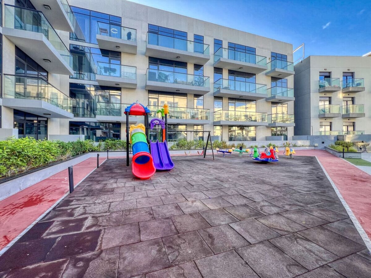 A playground with slides and swings in front of a modern building with balconies and large windows.