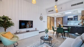 A modern living room with a flat-screen TV, comfortable seating, a dining area, and a kitchen. - Spacious 1BR Sleeps 4+Pool, Gym & Rooftop Terrace (دبي)