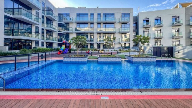 A modern hotel with a large outdoor swimming pool, multiple balconies, and a well-maintained garden area. - Spacious 1BR Sleeps 4+Pool, Gym & Rooftop Terrace (دبي)