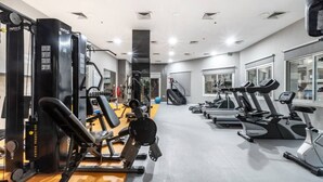 A gym with cardio machines, weightlifting equipment, and a mirrored wall. - Spacious 1-BR Opposite Mall with Huge Pool & Gym (Dubai)