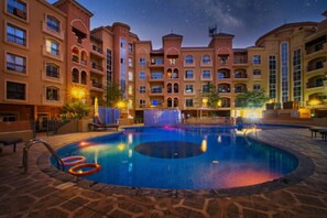 Una piscina rodeada de edificios de varios pisos con balcones, bajo un cielo nocturno estrellado.