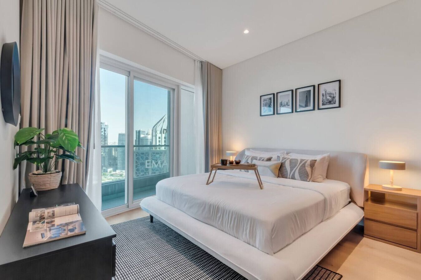 Een moderne hotelkamer met een groot bed, een bureau met een plant, uitzicht op de stad door het raam en een balkon.