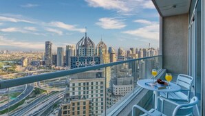 A balcony with a table and chairs, overlooking a cityscape with modern buildings and a highway. - Family & Group Friendly,  Near Beach Metro & Marina (Dubai)