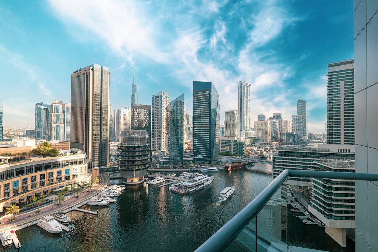 A high-rise building with a modern design, overlooking a marina with boats and a river.