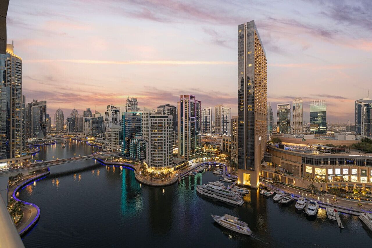 A modern cityscape with high-rise buildings, a marina with yachts, and a river.