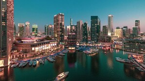 Eine Stadtansicht mit modernen Wolkenkratzern, einer Marina mit Booten und einer Uferpromenade.