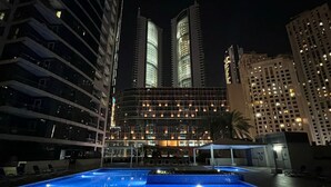Ein Hotel bei Nacht mit Pool, Hochhäusern im Hintergrund und einer gut beleuchteten Fassade.