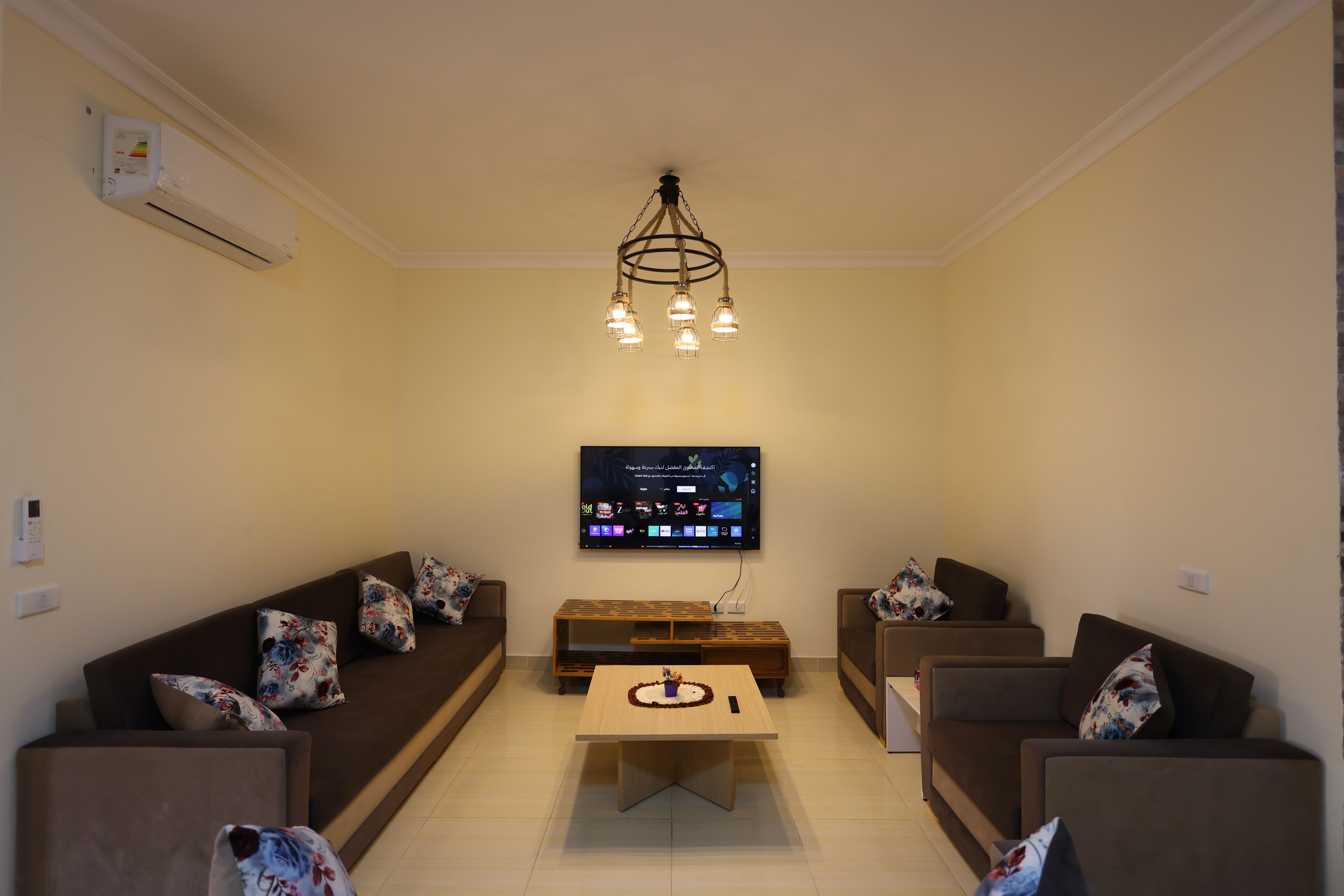 Een woonkamer met een flatscreen televisie, twee banken, een salontafel en een kroonluchter.