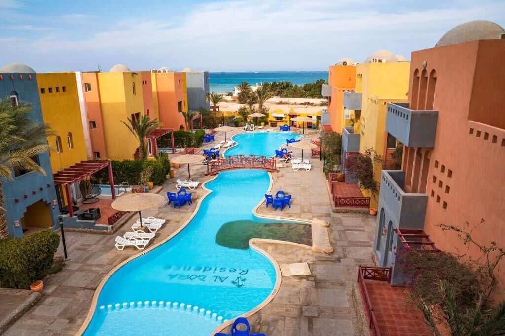 Een zwembad in een resort met een golvend ontwerp, omgeven door kleurrijke gebouwen en palmbomen.