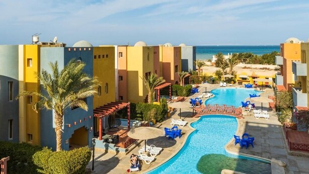 Um resort com piscina, palmeiras e vista para o mar.