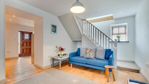 Een moderne woonkamer met een blauwe bank, een bijzettafeltje met een bloevas en een trap met een houten leuning.
