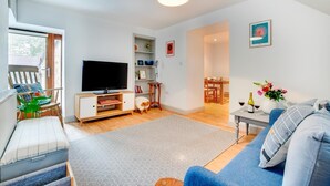 Een moderne woonkamer met een flatscreen-tv, een bank, een eethoek en een kleine tafel met een bloevas.