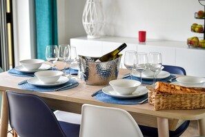 Une table à manger dressée avec des bols blancs, des verres à vin et une bouteille de champagne dans un seau en métal.