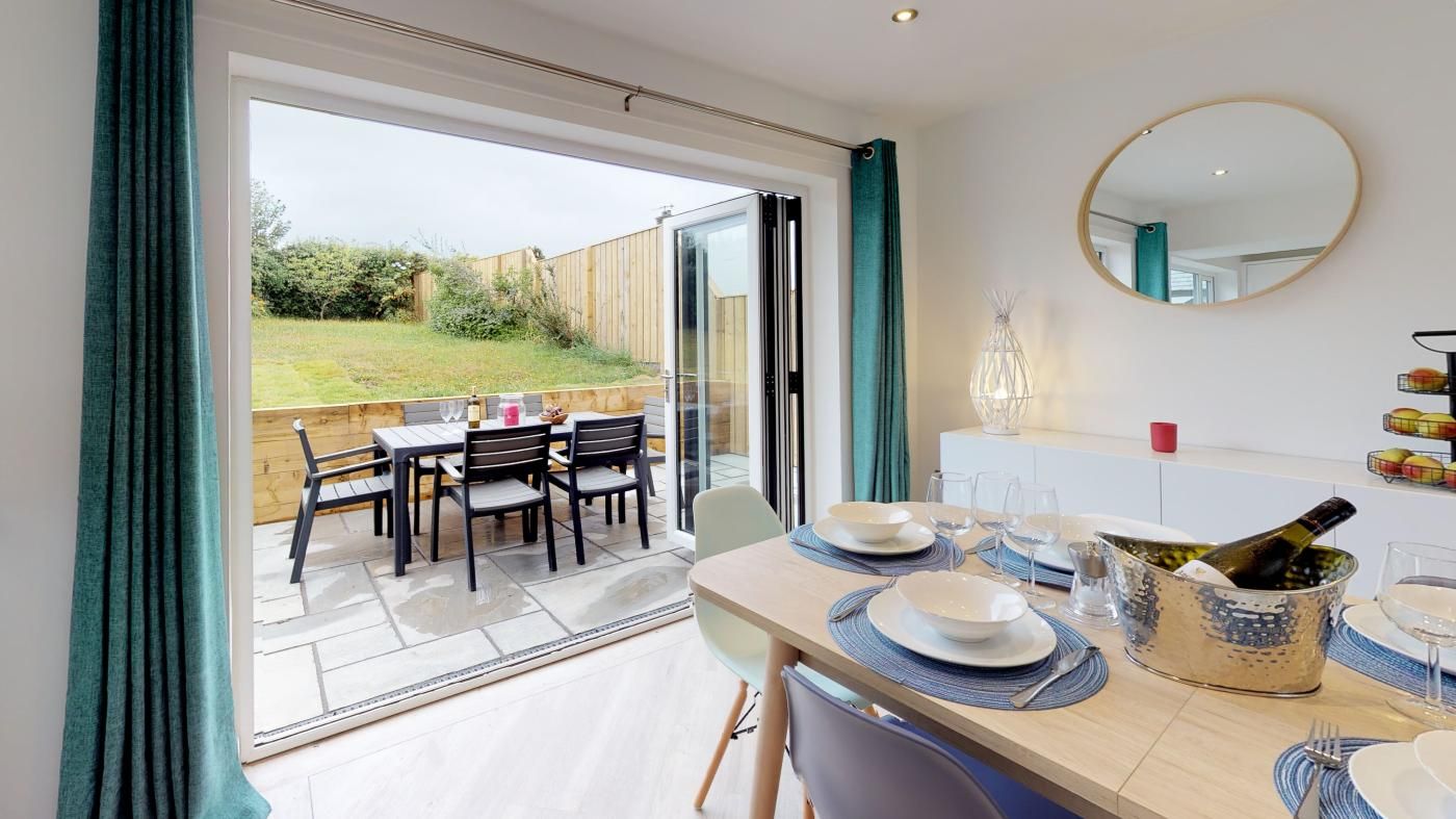A dining area with a table set for two, a bottle of champagne, and a view of a garden through a glass door.