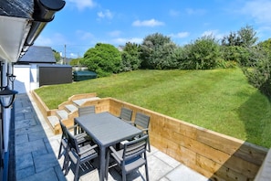 A patio with a table and chairs, surrounded by a wooden deck and a grassy lawn. - 2 Bed in Abersoch (oc-pendui) (Abersoch)