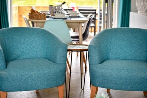 Two teal chairs with wooden legs, a small round table, and a dining table with chairs in the background. - 2 Bed in Abersoch (oc-pendui) (Abersoch)