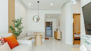 Un soggiorno moderno con un divano, un tavolino da caffè e una zona pranzo. Si nota una pianta, uno specchio e un televisore su un mobile.