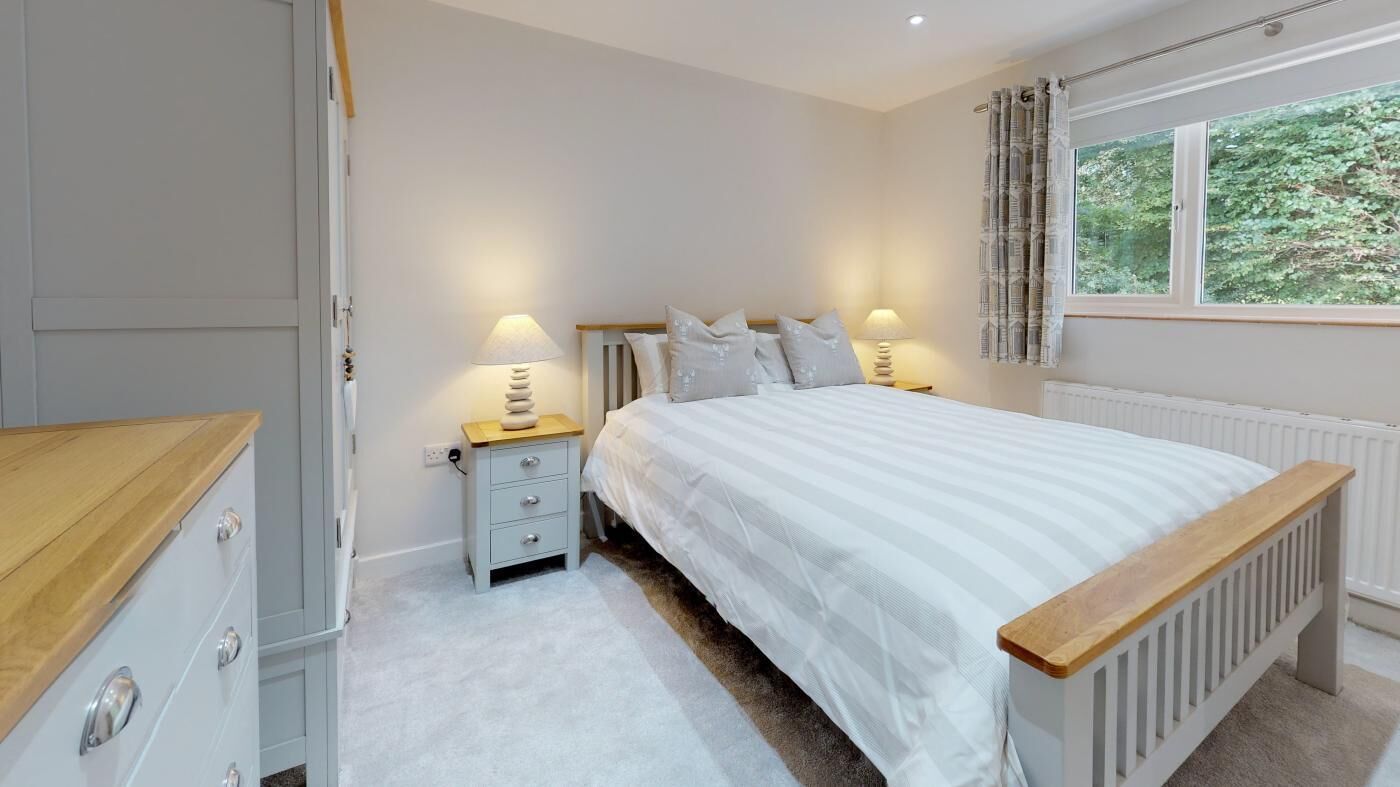 Une chambre à coucher avec un lit, des tables de chevet, une commode et une fenêtre avec des rideaux.