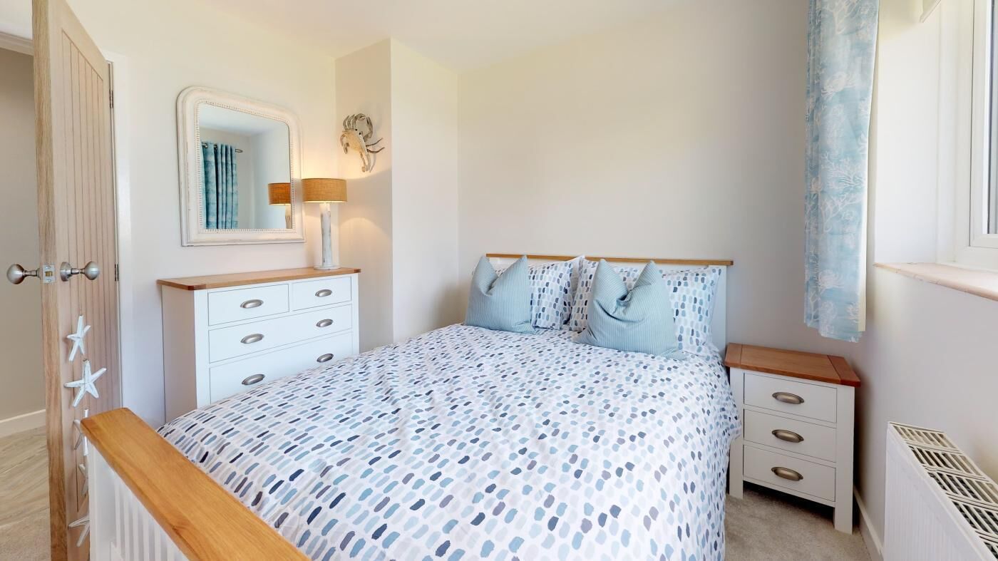 A bedroom with a bed, a dresser, a mirror, and a window with curtains.