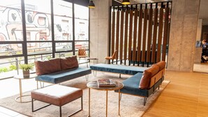 En moderne lounge med sofa, skabelon og runde borde, store vinduer med udsigt over byen og en træafskærmning.