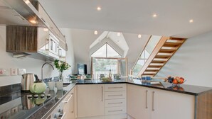 A modern kitchen with a central island, white cabinetry, and a wooden staircase. - 2 Bed in Looe (oc-p00778) (Looe)