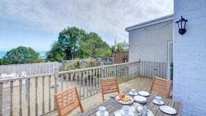En træterrasse med et bord dækket til morgenmad, med udsigt over en have og et vandareal.