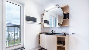 Een moderne badkamer met een gebogen spiegel, een zwart aanrechtbakje en een houten wastafelmeubel.