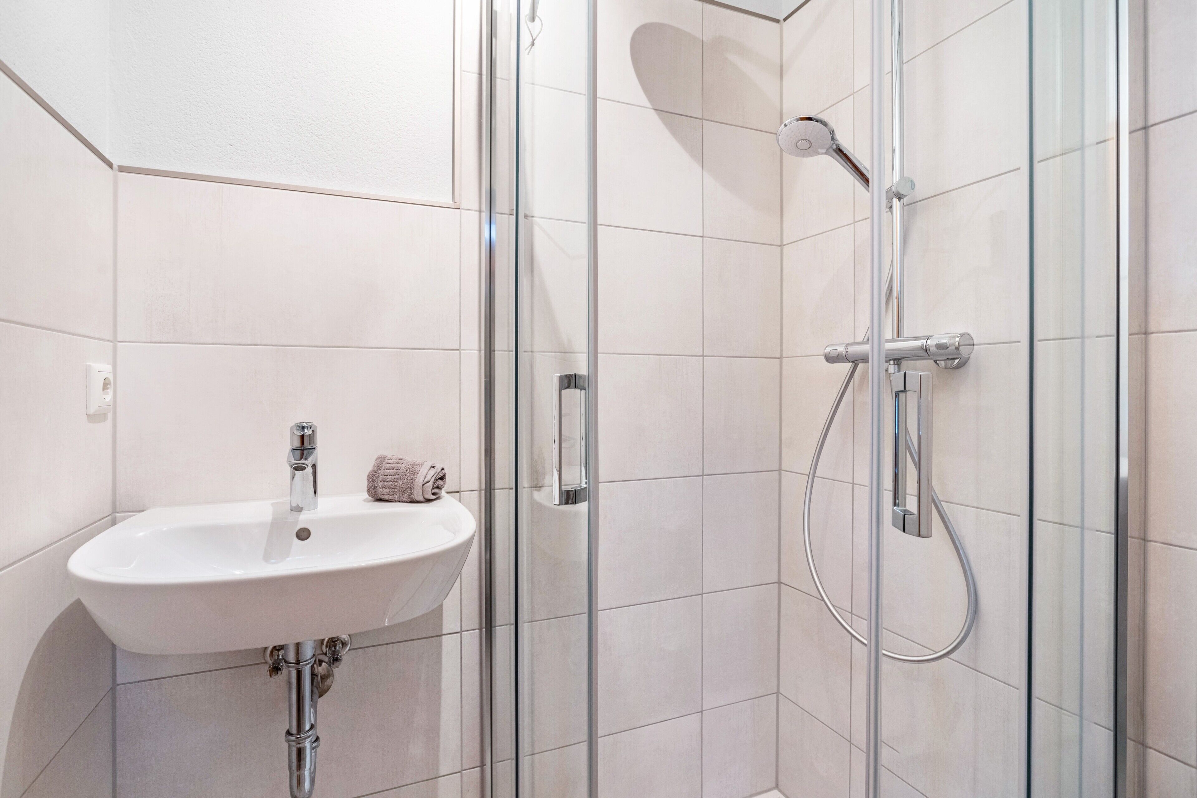 Un bagno con cabina doccia in vetro, un lavandino bianco e un asciugamano appeso al muro.
