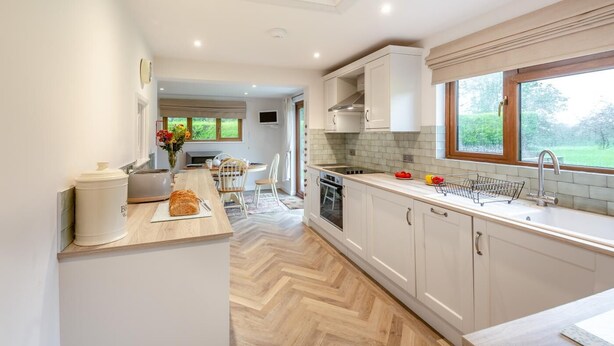 Une cuisine moderne avec des meubles blancs, un plan de travail en bois et une grande fenêtre offrant une vue sur l’extérieur.