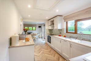 A modern kitchen with white cabinetry, a wooden countertop, and a large window providing a view of the outdoors. - 2 Bed in Pwllheli (oc-brynpe) (Pwllheli)