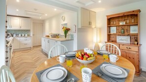 Une cuisine moderne avec des meubles blancs, un îlot central et un coin repas doté d’une table en bois, mise pour quatre personnes.