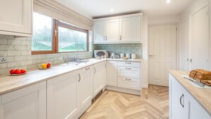 Une cuisine moderne avec des meubles blancs, un parquet en bois disposé en chevrons, une fenêtre offrant une belle vue et un plan de travail agrémenté d’ustensiles de cuisine.