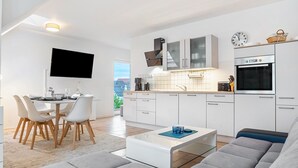 Ett modernt kök med vita skåp, en platt-TV och en matplats med bord och stolar.