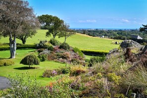 Un jardin aménagé avec différentes plantes et arbres, un mur de pierre et une vue sur une ville lointaine.