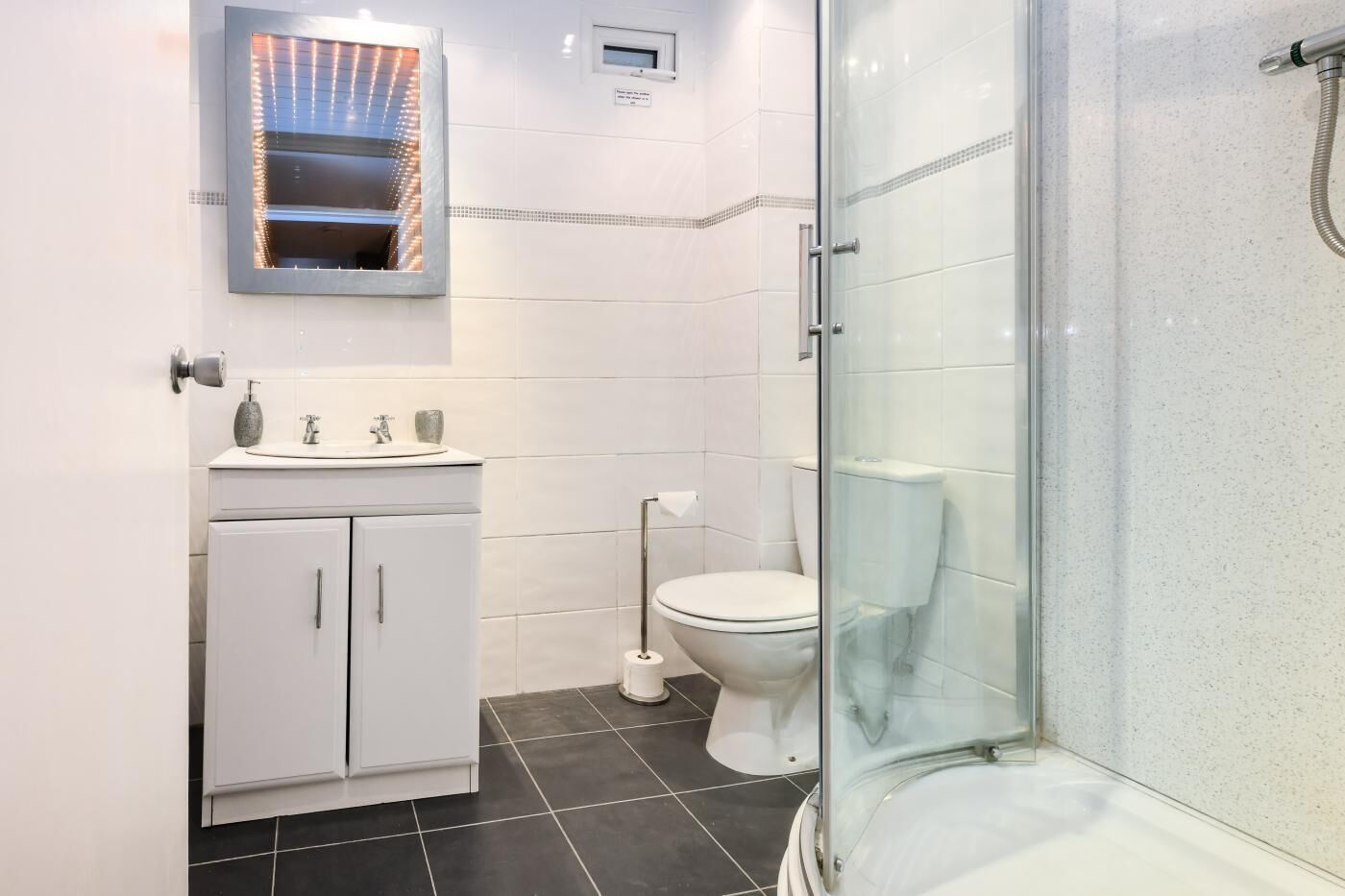 A modern bathroom with a glass shower enclosure, a white sink with a mirror above it, and a toilet.