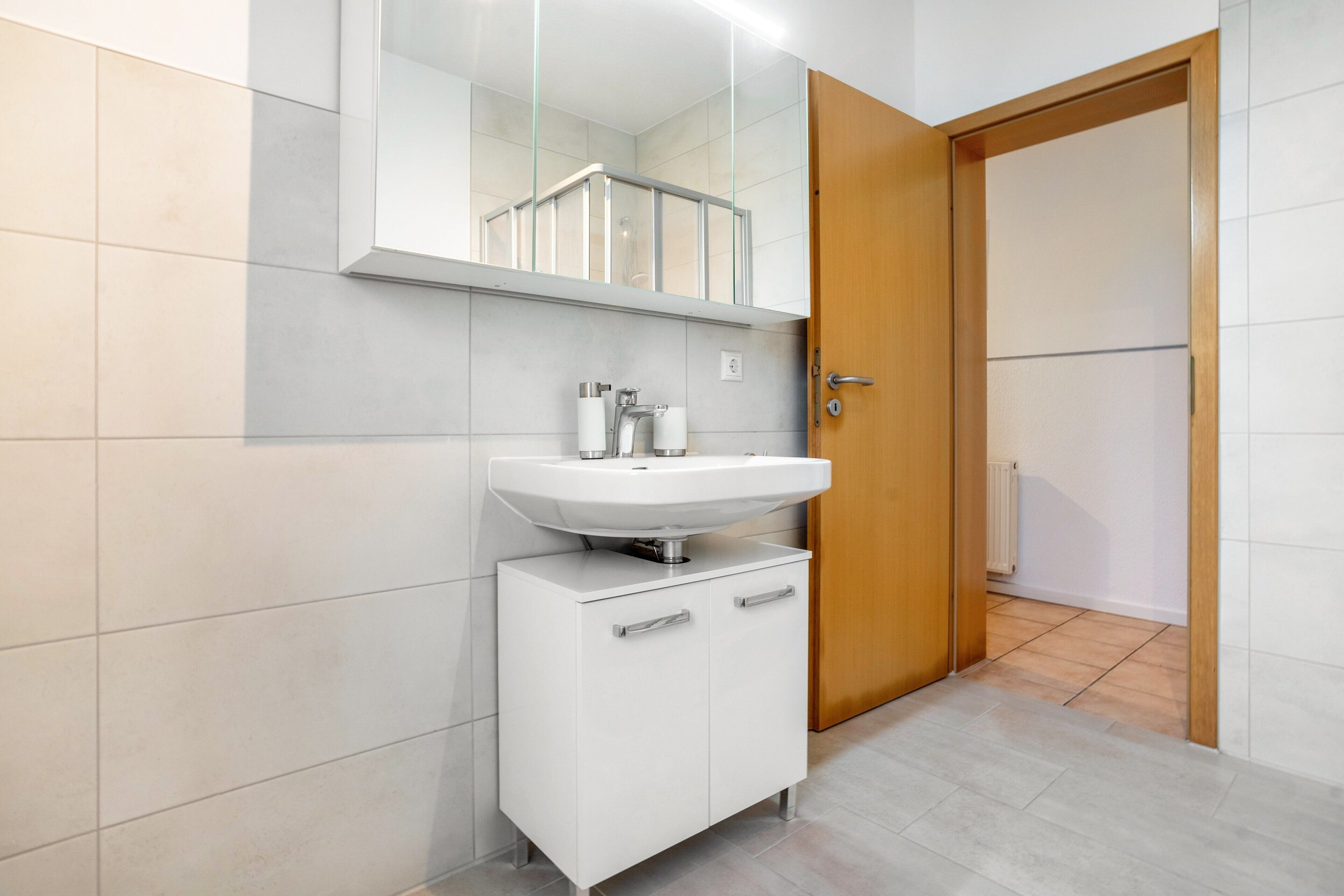 Un bagno con un lavandino bianco, uno specchio e una porta in legno.