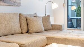 Un divano beige componibile con un tavolino rotondo, una lampada da terra e un quadro appeso al muro.