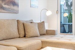 Ein beiges Ecksofa mit rundem Tisch, einer Stehlampe und einem Bild an der Wand.